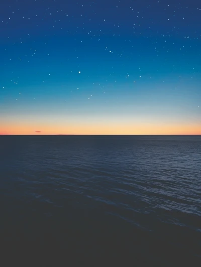 Sunset over calm ocean with starry sky