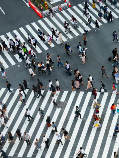 Aerial view of a busy pedestrian crossing with many people walking across white striped crosswalks on a city street